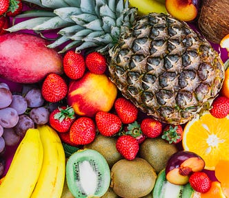 Close up photograph of vibrantly coloured fruit: grapes-strawberries-pineapple-kiwi-apricot-banana-whole-pineapple