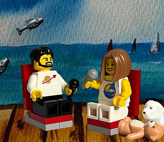 Beach with boats and author and Andi in LEGO minifig form on the peer with microphones in their hands, conducting the interview.