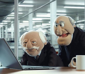 Two old men looking at a laptop with grouchy expressions on their faces. The two old men are Statler and Waldorf, who are puppets on The Muppet Show.