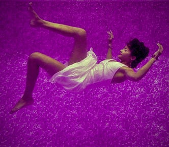 Letting Go- a woman is gently falling against a purple backdrop with a calm demeanor and smile on her face