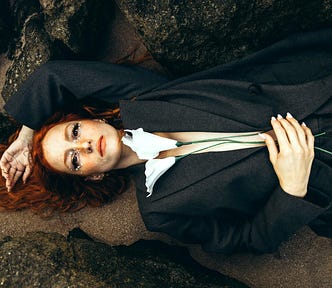 A woman is lying on sand while holding flowers.