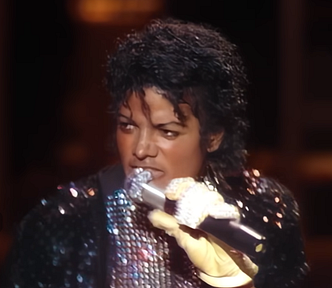 Michael Jackson signing in a sequin jacket with one glove on his left hand.