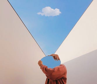 A photo of a person holding a mirror that reflects the blue sky. The mirror is covering their face.