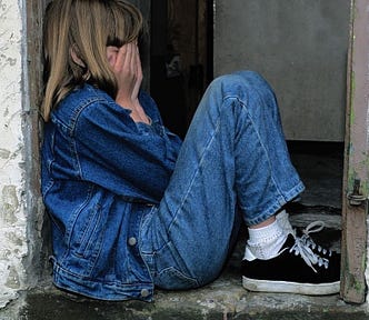 child sitting in a doorway, hands covering face