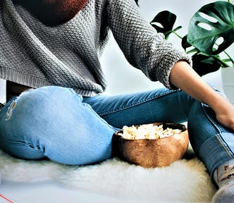 girl wearing grey sweater and blue jeans eating bowl of popcorn
