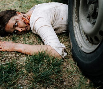 A woman with zombie eyes lies beside a car tire