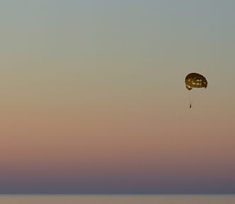 Parasailing perspective: fearless, sunset with boats and paddle surfers on a calm waterfront as a parasailor flies in the sky above