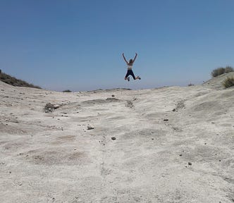 A woman jumps out of joy on a sandy trail along the beach.