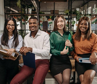 One back man, two white ladies, and one black lady sitting on a desk