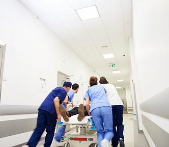Hospital staff rush a patient down a hospital hallway on a gurney.