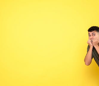 Man with his fists by his open mouth as if biting his nails. He looks very worried, but in an amused way. Bright yellow background
