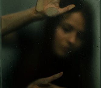 Image of a woman in a small space, apparently trapped behind glass