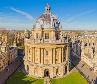 Large stone domed library on campus of Oxford University in England on green grass beneath blue sky
