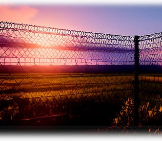 Light from a setting sun comes through a chain link fence.