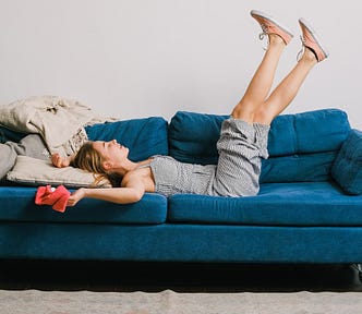 Woman lying on a blue couch with her legs thrown up in the air and her arms back.