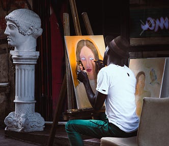 A Black man sits in a room painting a portrait of a woman. On the side of the room is a statue with a bust of a man on top of it.