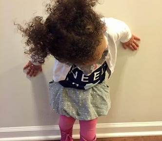 Small toddler with curly hair standing against a white wall looking down