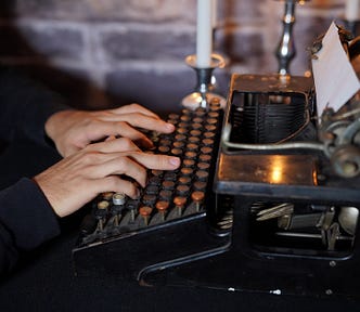 Color photo of a man typing on an older typewriter.