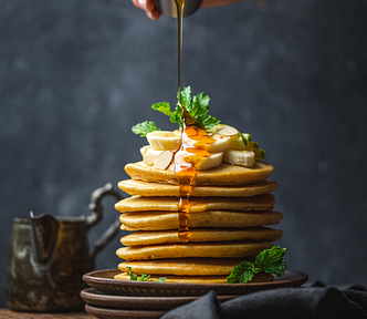 A pile of pancakes on a plate with a sliced banana on top drizzled with maple syrup