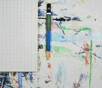 A blank grid notebook laying open on a paint-splattered desk with a pencil next to it.