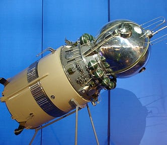 Color photograph of a model of the Vostok 1 spacecraft set against a blue background