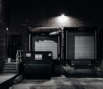 Loading dock and dumpster illuminated by a spotlight.