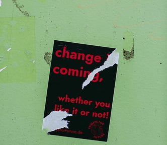 The sign says “change is coming, whether you like it or not.” It’s a tad ripped and is on a green wall.