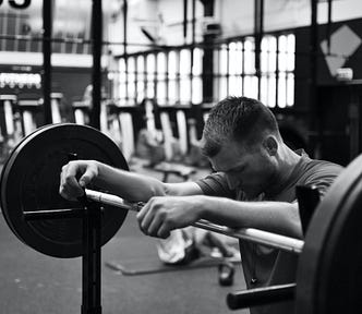 Man resting arms against a barbell of weights in a large gym