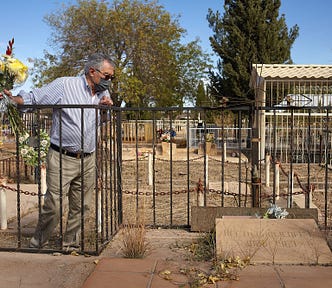 An 80 year old man holds a flower bouquet in his hand as he bends over a small fence to observe his father’s grave to which he hasn’t been to visit in almost 30 years. It is a cold and sunny day in winter at Cananea, Sonora’s cemetery. Most of the graves there are abandoned.