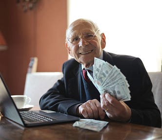The is shows a senior person who works remotely, showing his earning as dollar bills in his hands. He looks proud of his earning.