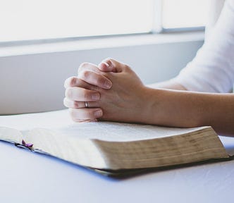 Woman praying, with hands folded over an open Bible