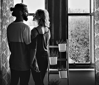 black & white photo of couple looking at each other in front of window