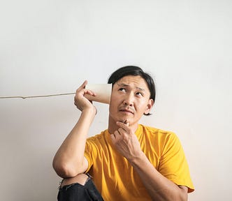Pensive Asian man with Yellow shirt on listening on a cup phone