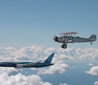 A modern jet and an old biplane flying above clouds
