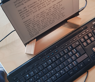 The reMarkable 2 tablet on a desk on a wooden stand. The keyboard is in front of it.
