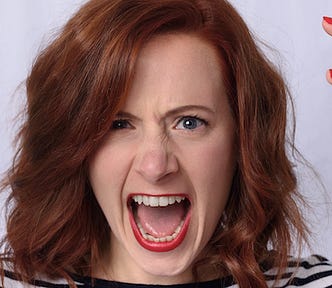 Close up of an angry red-haired woman with red lips, and open mouth with teeth bared.