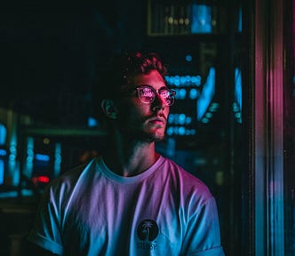 Man wearing glasses, looking at a neon sign.