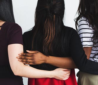 Three women interlace arms behind each other’s backs.