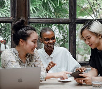 Three young, diverse people looking at the screen of the smartphone held by one of them.