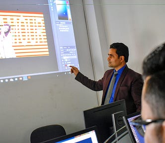 A man in a suit gesturing to a terribly designed picture while employees watch on.