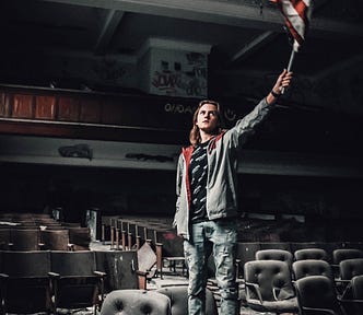 Young man waving an American flag in an old decaying empty theatre.