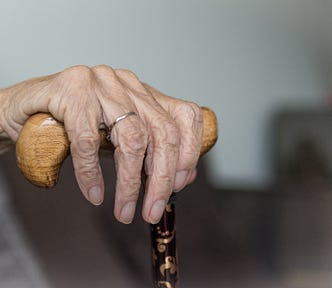 An elderly woman’s hand rests upon the top of a cane.