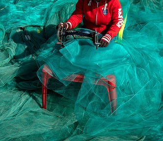 A young woman sits sewing huge billowing nets.