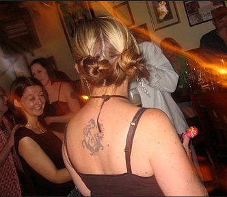 Woman with bleached pigtails and a back tattoo in a bar.