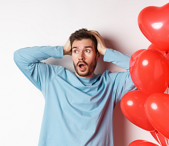 Boyfriend grabs his head with his hands in a panic about Valentine’s Day, heart balloons next to him, an alarmed look on his face.