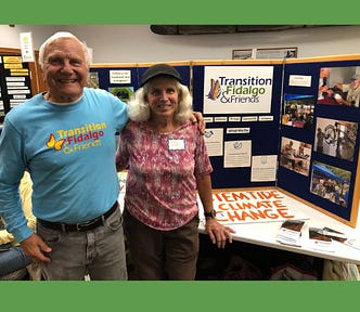 An image of a gray haired man and woman in front of a display with a poster saying ‘Transition Fidalgo & Friends’ and ‘Stem the tide of climate change’.