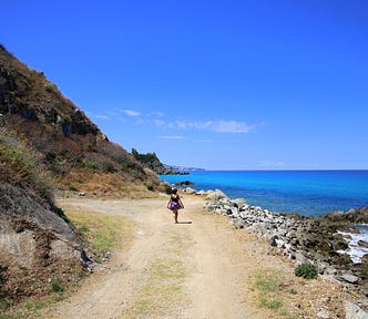 The author is walking away from the camera, the sea on the right side and dramatic cliffs on the left. Calabria, Italy.