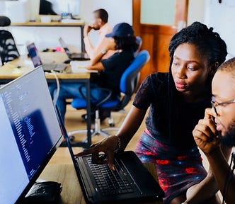 A mentor aside her mentee pointing at something on his laptop screen.