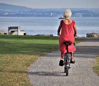 Image of pensioner wearing red dress & riding a bike by pasja1000 on Pixabay