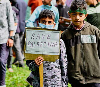 A boy holds a handwritten sign that says “Save Palestine.”